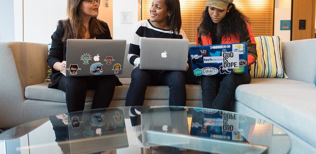 [IMAGE] Three women sat next to each other, talking. All three have laptops on their knees. Some of the laptops have stickers on them.