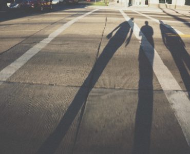 [IMAGE] White lines painted on a road. Three shadows of people originating from near the camera are cast across the road and one of the lines