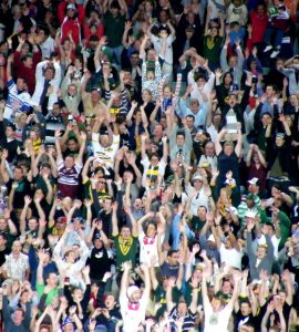 [IMAGE] A crowd of people at a sports game with their arms raised above their heads, doing the wave