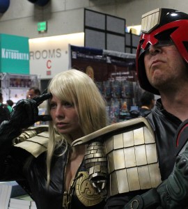 man dressed as Judge Dredd with a blonde woman saluting behind him dressed as Anderson, at San Diego ComicCon