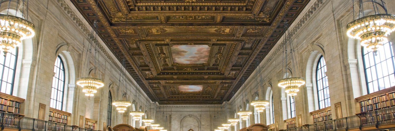 [IMAGE] The New York Public Library main branch reading room. People seated at large desks under a painted ceiling with window lined walls