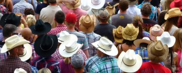 [IMAGE] A large crowd of people facing away from the camera. They are all wearing hats, mostly cowboy or straw hats. You cannot see anybody's faces.