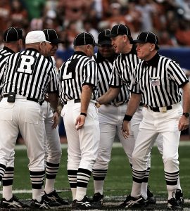 [IMAGE] A group of American Football referees in striped jerseys are having a conversation