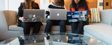 [IMAGE] Three women sat next to each other, talking. All three have laptops on their knees. Some of the laptops have stickers on them.