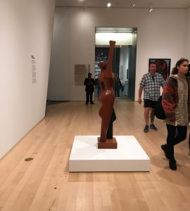 Museum powers walk past statue of a woman holding up a fist in the Brooklyn Museum