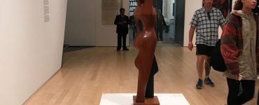 Museum powers walk past statue of a woman holding up a fist in the Brooklyn Museum
