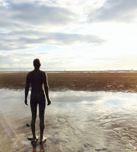 A statue stands on a beach looking out towards the horizon